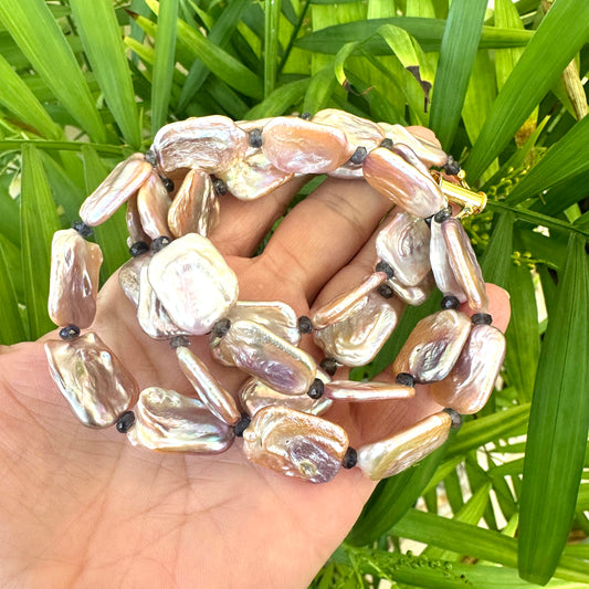 Statement Pearl Necklace with pink rectangular pearls and navy iolite gemstones held in hand against green background.