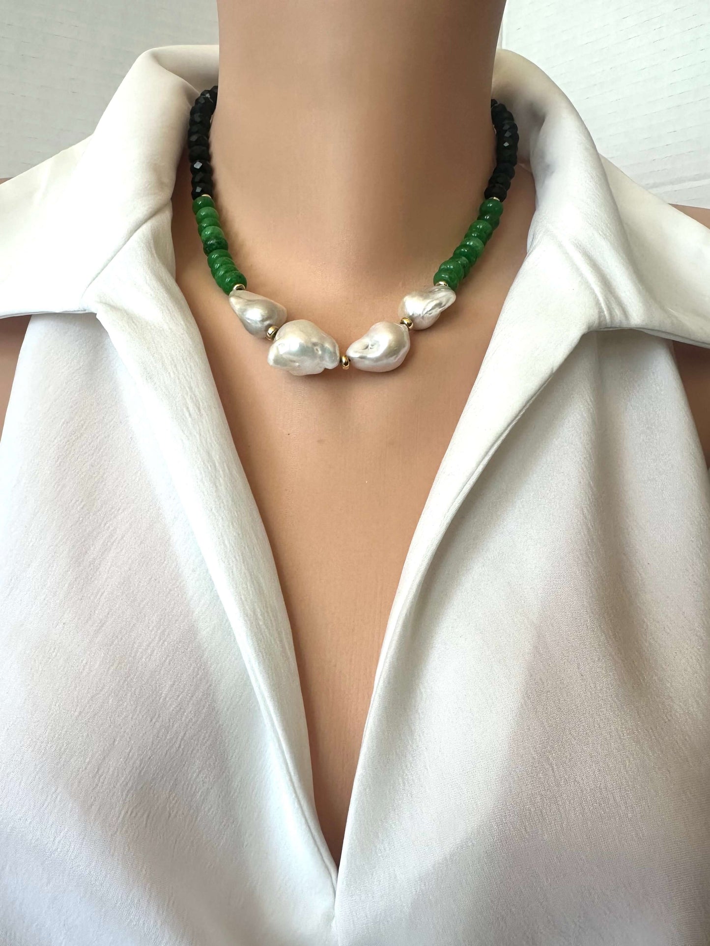A close-up of a necklace worn on a mannequin or model torso, featuring 4 large irregular white baroque pearls in the center, flanked by green beads and black beads, styled with a white collared shirt.