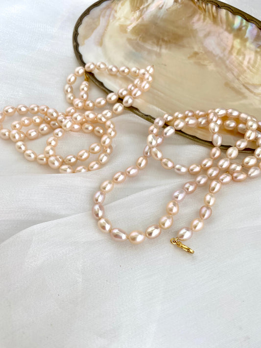 Pearl necklace on a white surface with an open shell in the background