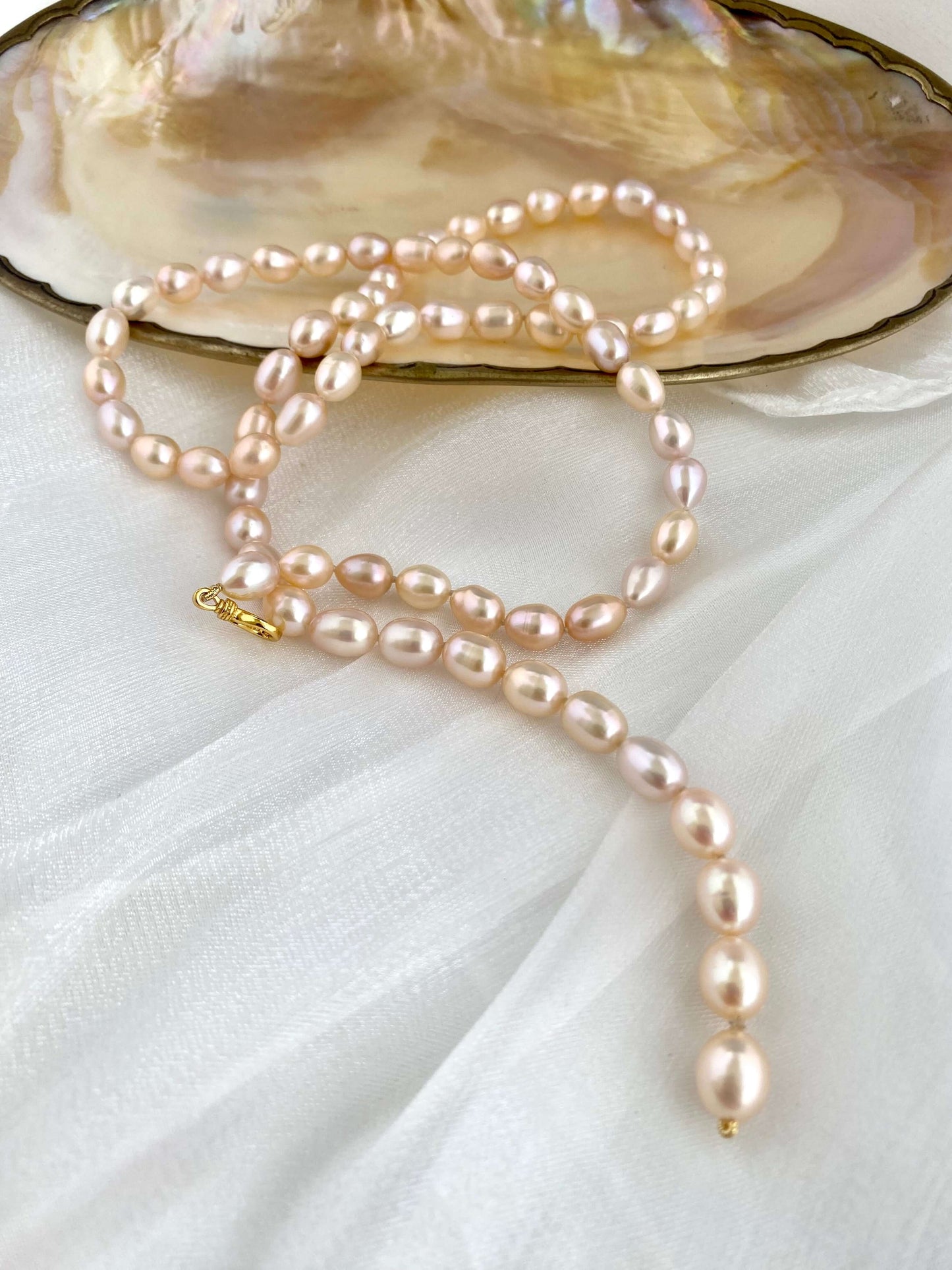 Pearl necklace draped over an open shell on a white fabric background