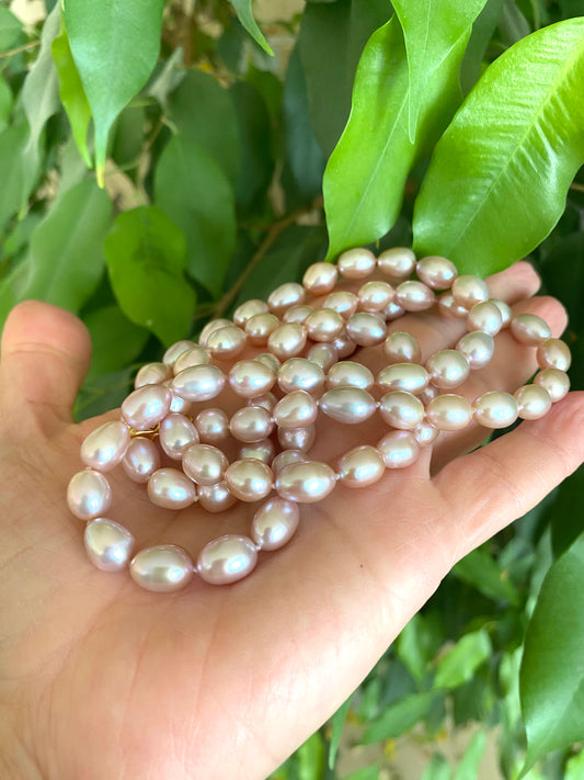 Pearl necklace held in a hand with green leaves in the background