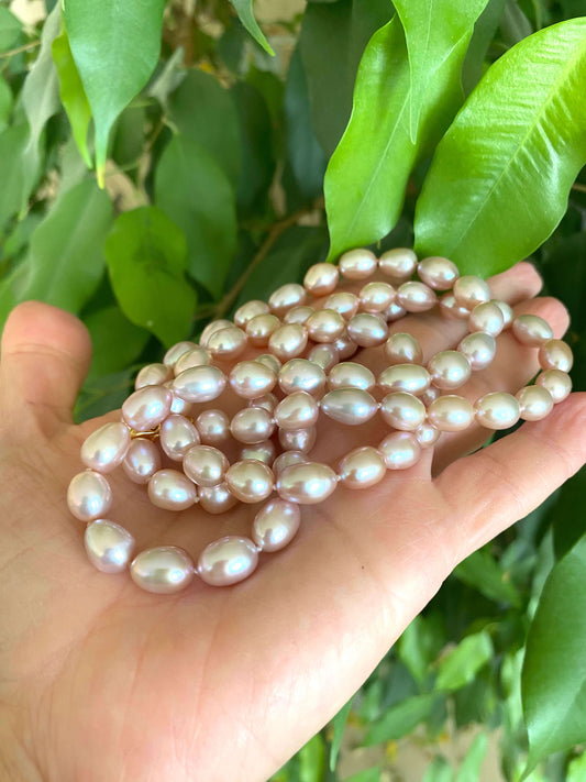 Pearl necklace held in a hand with green leaves in the background