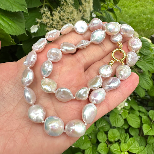 Close-up of coin pearl necklace held in hand against summer foliage
