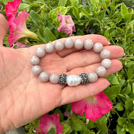 Pink jade pearl bracelet held in hand against green foliage