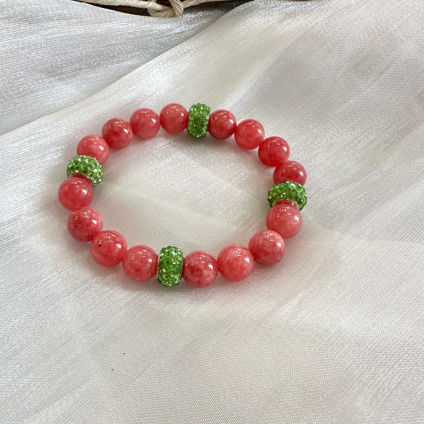 Red jade bracelet without pearl and green rhinestones displayed on white cloth