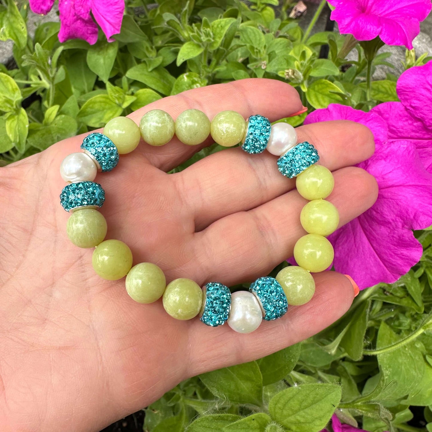Olive green jade bracelet with three pearls held in hand near pink flowers