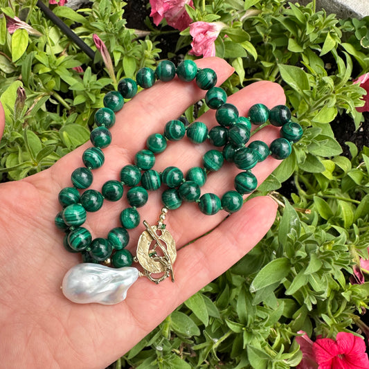 Malachite toggle necklace with baroque pearl pendant displayed in a hand, showcasing vibrant green gemstones.