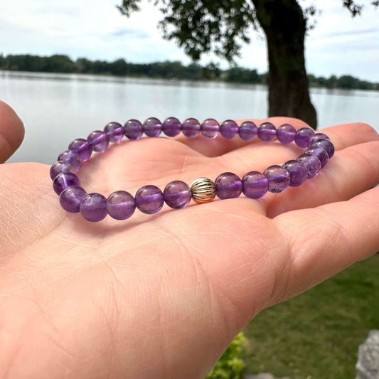 Amethyst bracelet held in hand against lake and green foliage