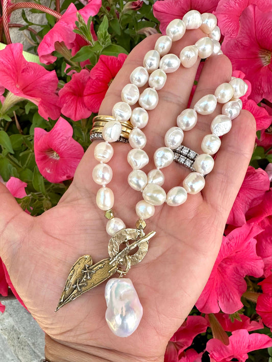 Close-up of pearl toggle necklace with heart pendant held outdoors