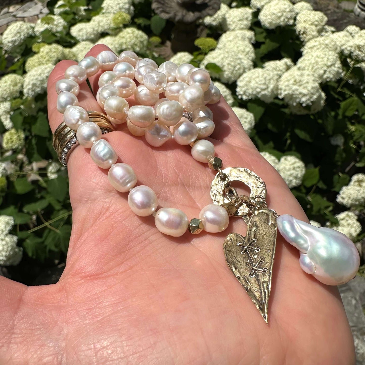 Pearl toggle necklace with heart pendant held in hand against natural foliage