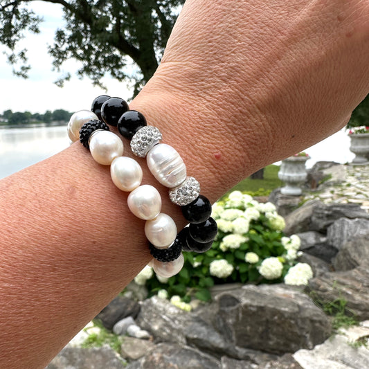 Two white pearl stretch bracelets with black rhinestones worn on woman's wrist in summer foliage