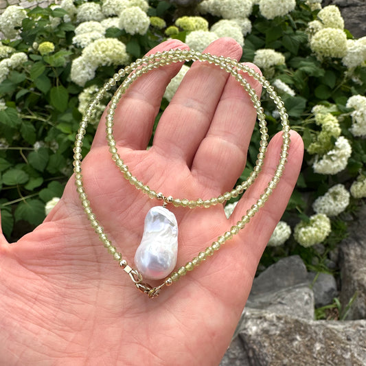 Peridot beaded necklace with baroque pearl pendant held in hand against green foliage