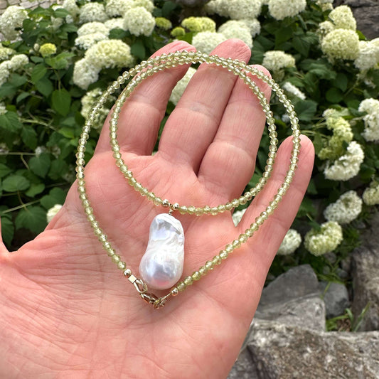 Peridot beaded necklace with baroque pearl pendant held in hand against green foliage