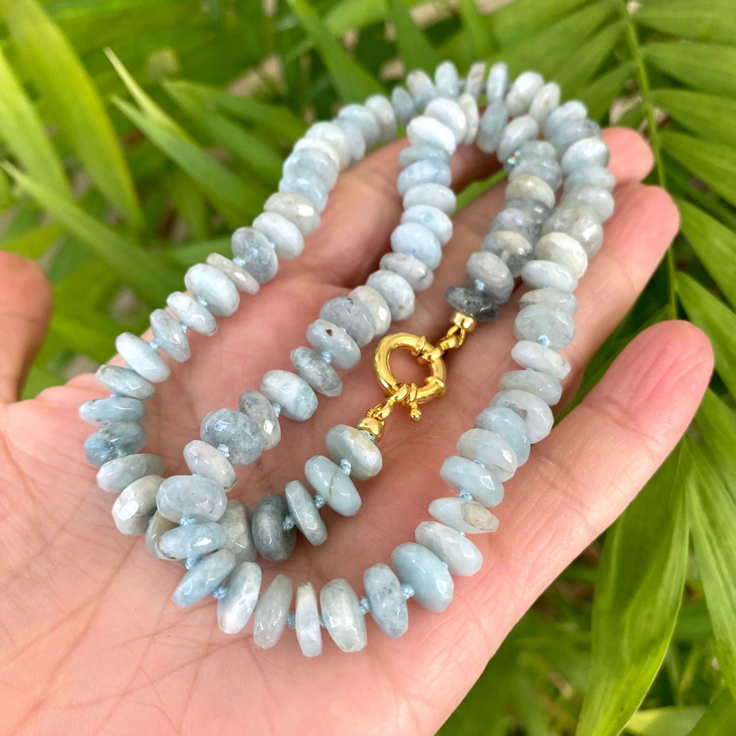Aquamarine beaded necklace held in hand against green leaves