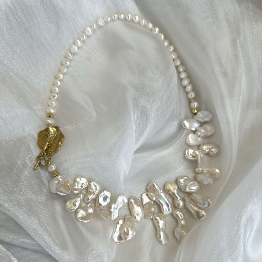 Close-up of white petal pearl necklace on white fabric highlighting asymmetrical pearls