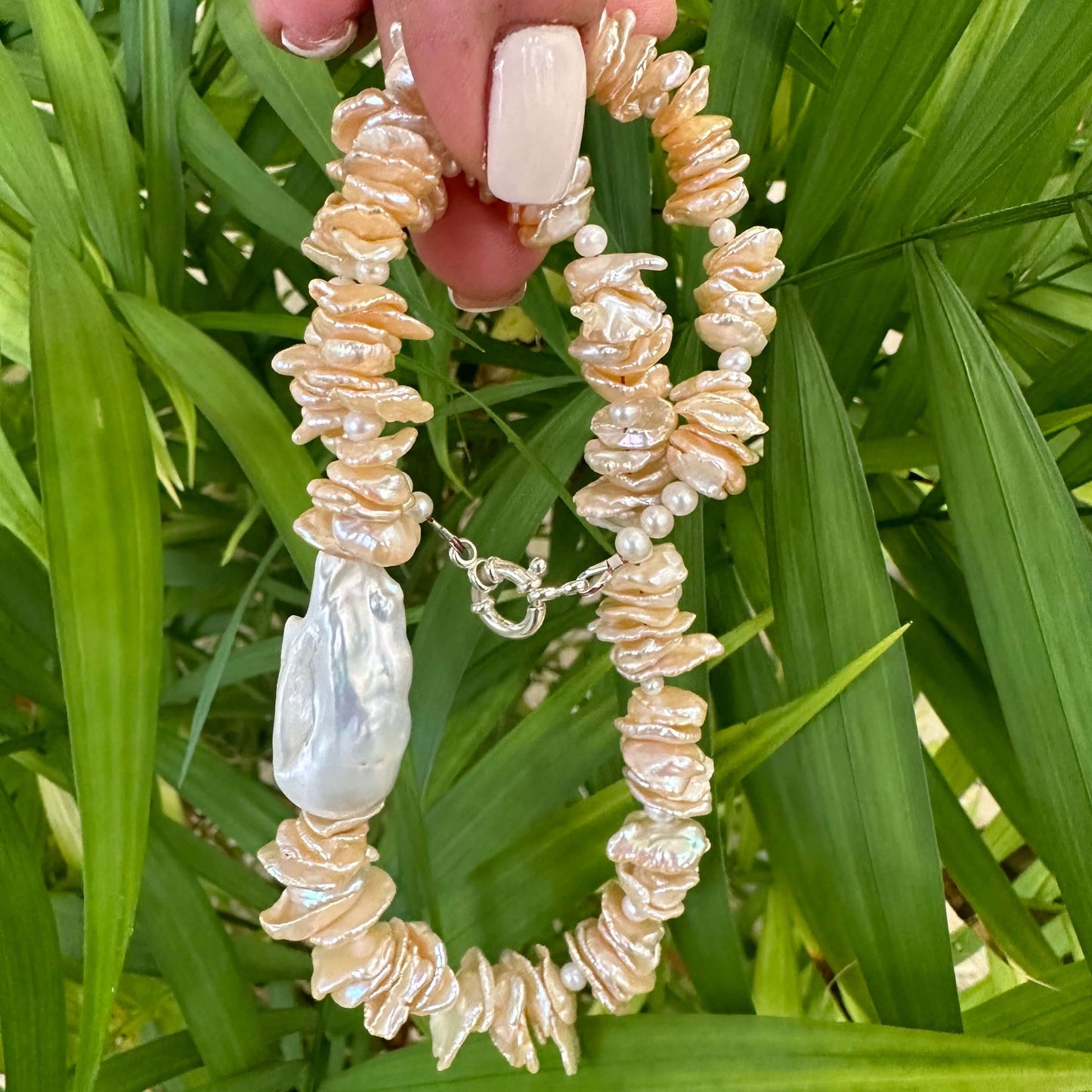 Peach keshi pearl necklace held in hand against green leaf backdrop showing luster and texture