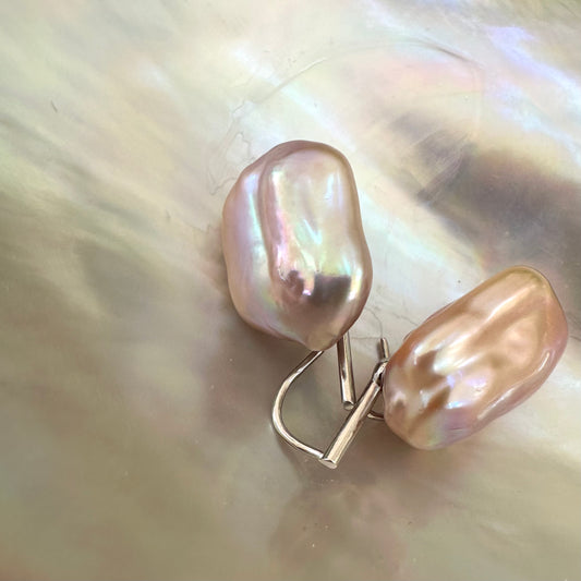 Purple pearl drop earrings with rectangular baroque pearls on white shell, showing pink-lavender hue and natural iridescence.