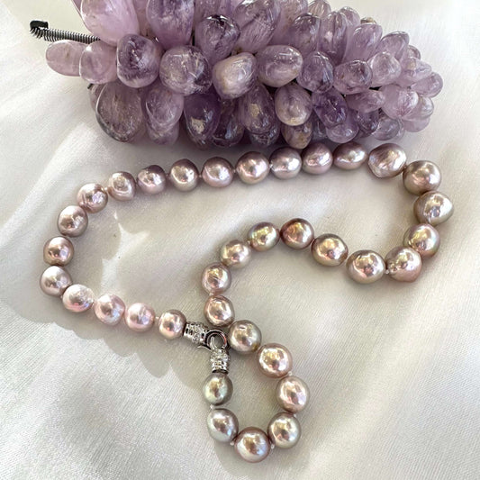 Pink lavender pearl necklace displayed on white cloth beside amethyst crystal ornament, showing elegant color contrast.