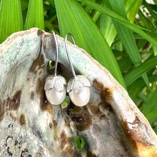 Cargar imagen en el visor de la galería, Rice Pearl Earrings – silver pair close-up on pearl shell and green foliage