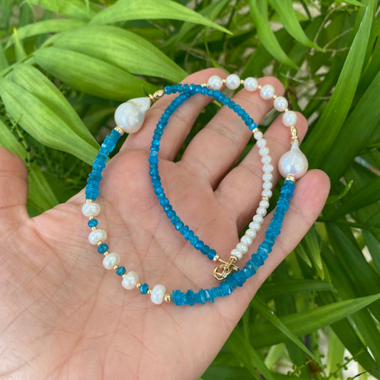 Blue Apatite Baroque Pearl Necklace | Asymmetric 14K Gold Filled on a hand surrounded by green foliage.