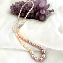 Carica l'immagine nel visualizzatore di Gallery, Rice Pearl Necklace with pastel pearls arranged beside amethyst ornament on white fabric background.