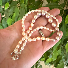 Carica l'immagine nel visualizzatore di Gallery, Handcrafted Rice Pearl Necklace with pastel pearls held in hand against green leaf background.