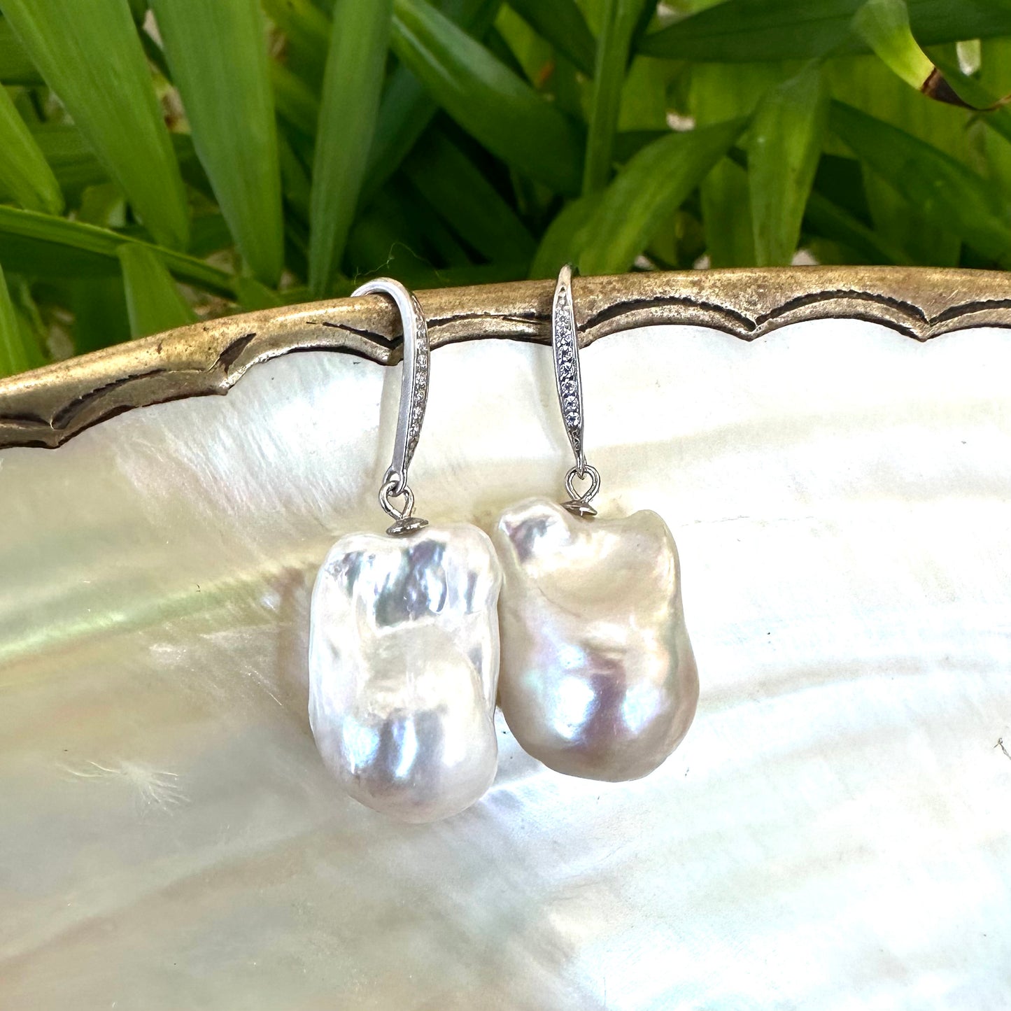 White baroque pearl bridal earrings displayed on pearl shell with green leaves, designed and handmade in Canada.