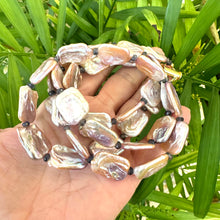 Load image into Gallery viewer, Statement Pearl Necklace with pink rectangular pearls and navy iolite gemstones held in hand against green background.