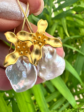 Carica l'immagine nel visualizzatore di Gallery, Keshi Pearl Earrings with white petal pearls and gold vermeil flower hooks held in hand against green leaf background.