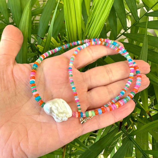 Hand holding opal and baroque pearl necklace near green leaf background