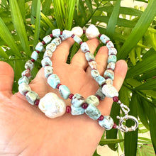 Lade das Bild in den Galerie-Viewer, Hand holding larimar ruby and baroque pearl necklace near green leaf background