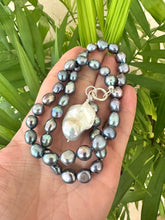 Cargar imagen en el visor de la galería, Hand holding black pearl necklace with baroque pendant near green leaf background