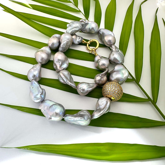 Silver grey baroque pearl necklace close up on green leaf background