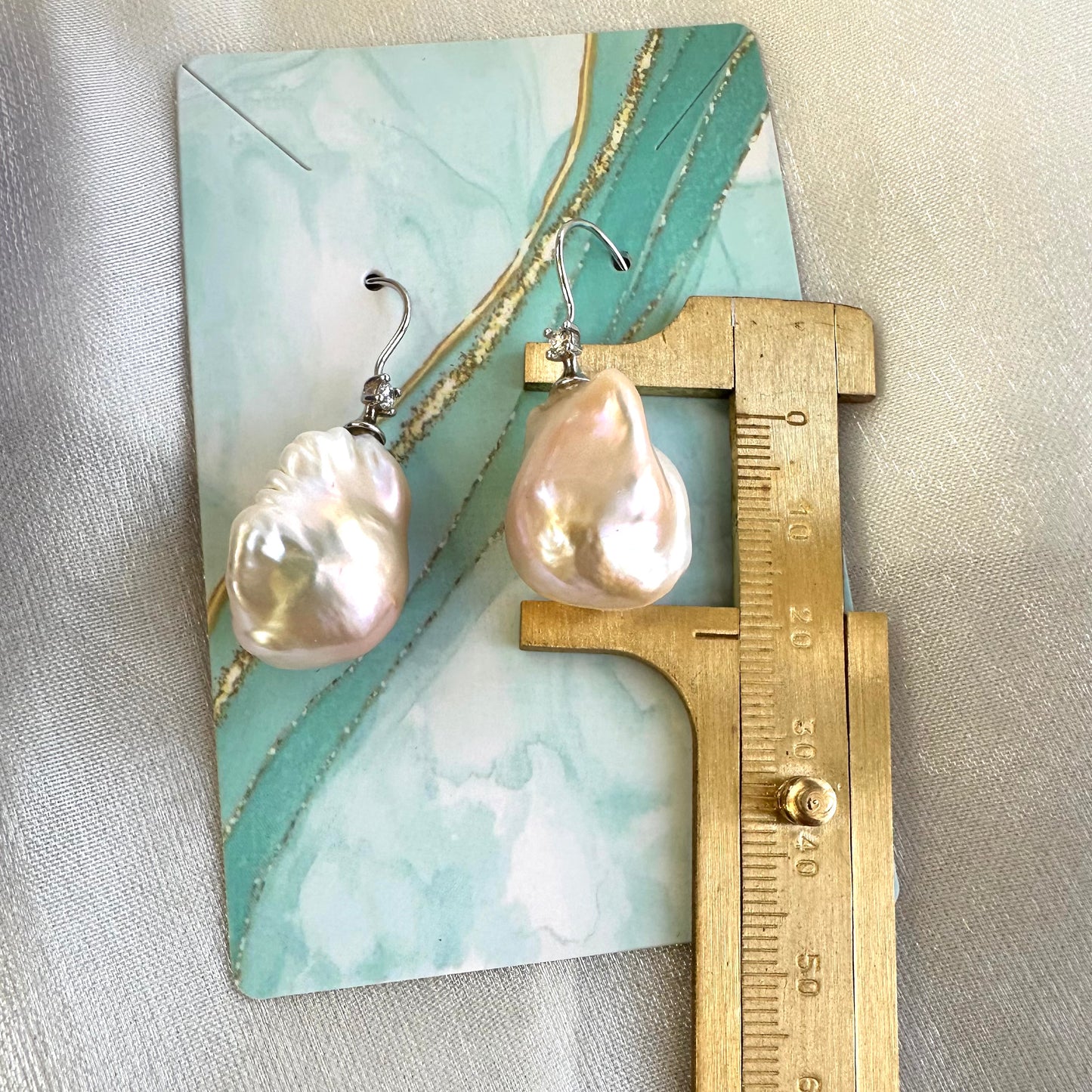 Golden Baroque Pearl Earrings – measured for size against turquoise backdrop with ruler