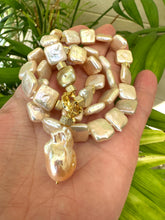 Carica l'immagine nel visualizzatore di Gallery, Hand holding golden baroque pearl toggle necklace against leafy green background — lustrous baroque pearls and gold details by Loulia Pearl Jewelry