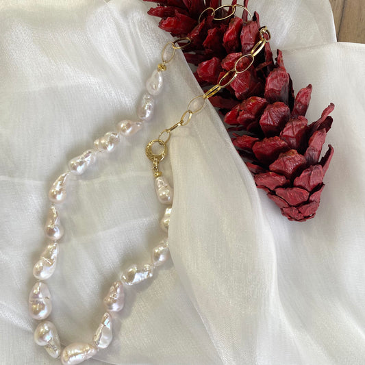 White baroque pearl and gold chain necklace resting on white cloth with red pine cone, elegant handcrafted jewelry from Canada.