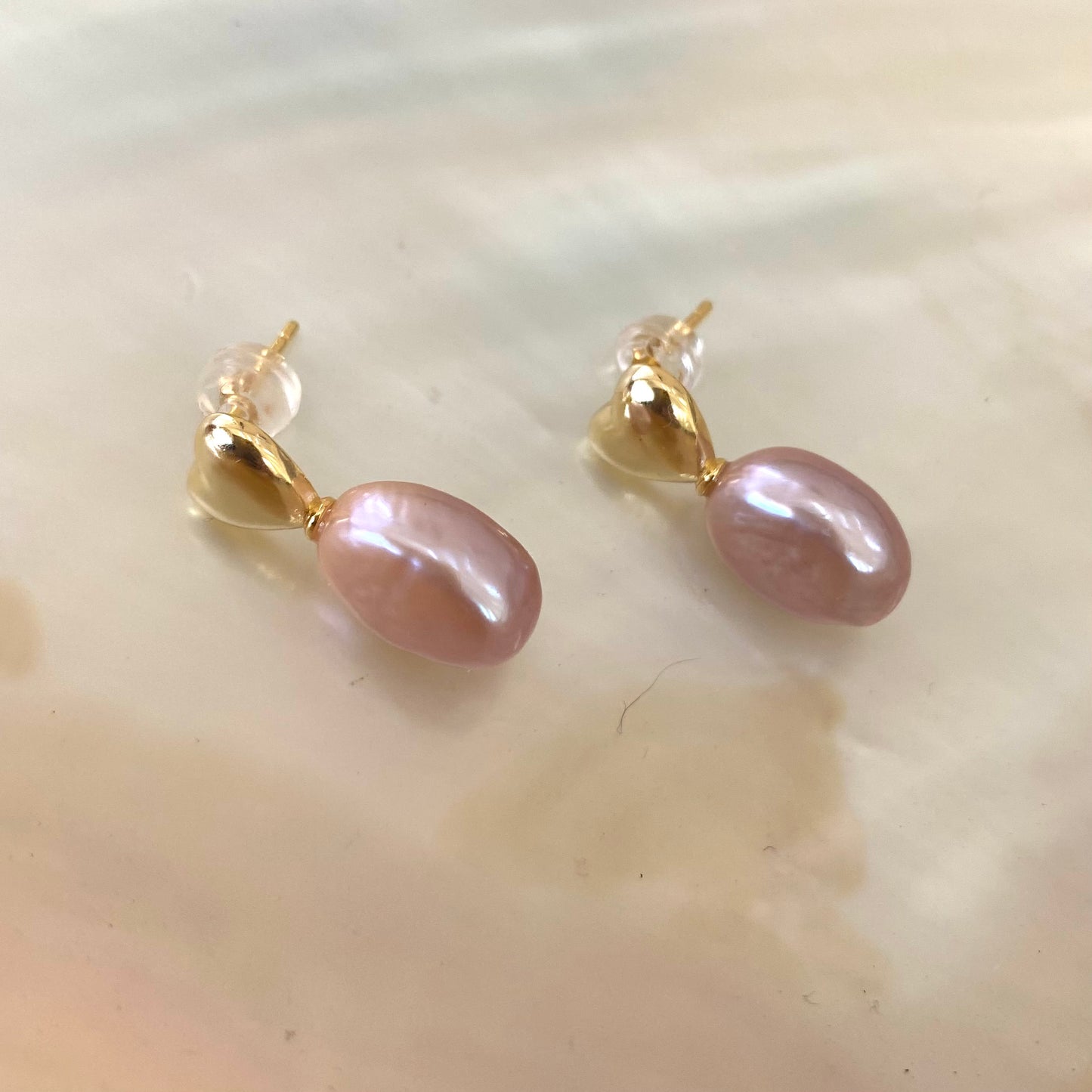 Heart Pearl Earrings – gold version close-up against white pearl shell
