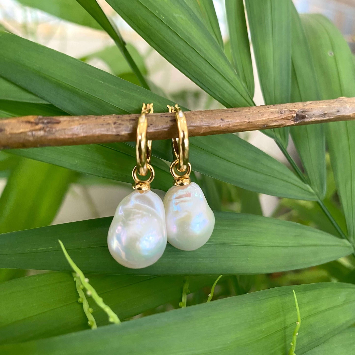 White Baroque Pearl Earrings – gold dangle design shown on green leaf background