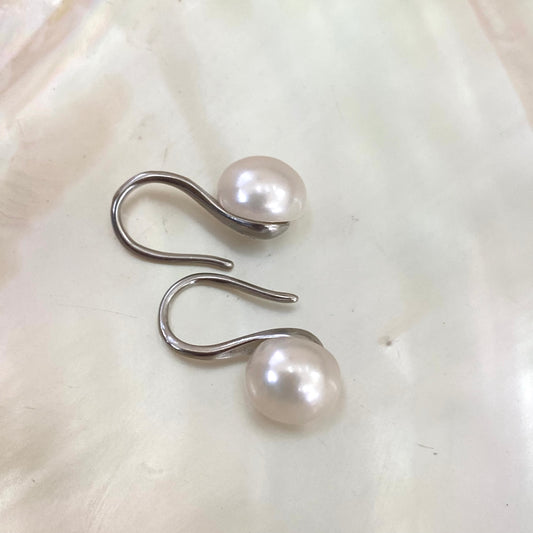 Button Pearl Earrings – silver version close-up against white pearl shell background