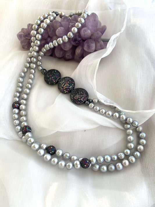 Grey Pearl Necklace with double strands of pearls arranged beside amethyst ornament on white fabric background.