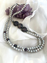 Carica l'immagine nel visualizzatore di Gallery, Grey Pearl Necklace with double strands of pearls arranged beside amethyst ornament on white fabric background.