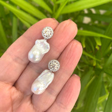 Lade das Bild in den Galerie-Viewer, Moissanite and baroque pearl earrings held in hand against green leaves, handmade jewelry display.