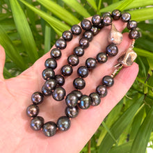 Carica l'immagine nel visualizzatore di Gallery, Black pearl necklace with rose gold pendant held in hand against green leaf backdrop