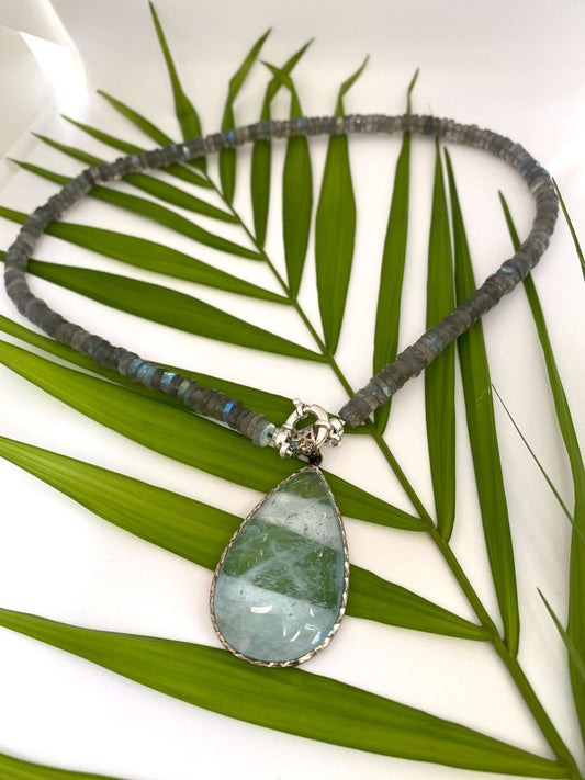 Labradorite aquamarine pendant necklace displayed on leafy branch backdrop — natural light gemstone jewelry by Loulia Pearl Jewelry
