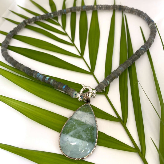 Labradorite aquamarine pendant necklace displayed on leafy branch backdrop — natural light gemstone jewelry by Loulia Pearl Jewelry