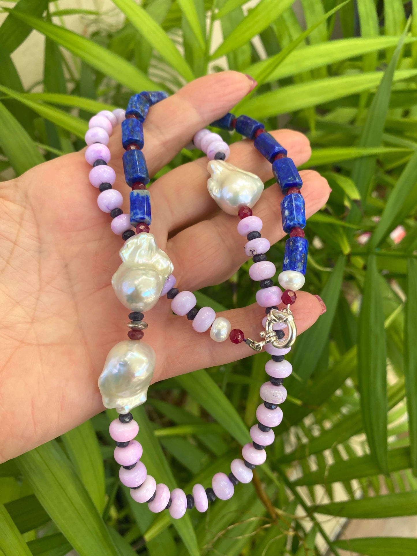 Handcrafted lapis lazuli opal agate pearl necklace photographed outdoors with green leaves — artistic gemstone jewelry design by Loulia Pearl Jewelry