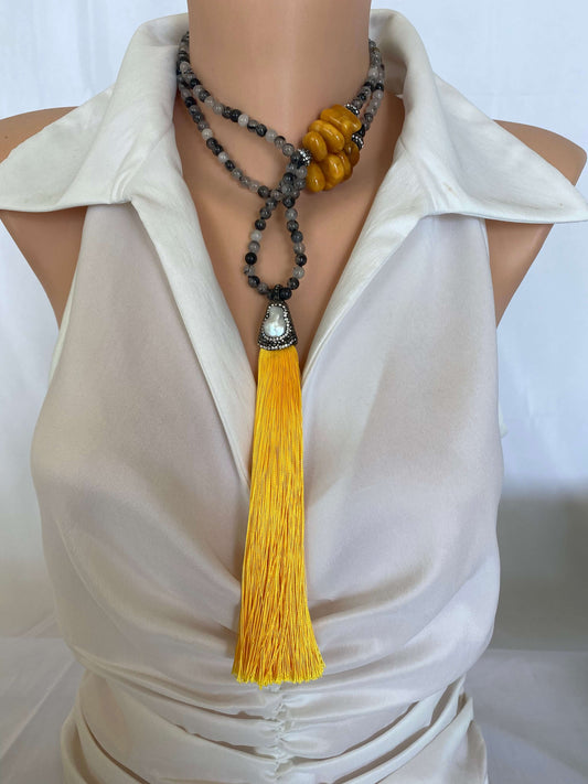 Boho rutilated quartz necklace with yellow copal tassel on mannequin, frontal medium shot.