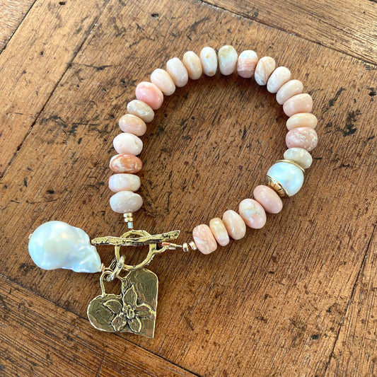 Pink opal bracelet with heart and baroque pearl charm showcasing artisan craftsmanship and natural beauty.
