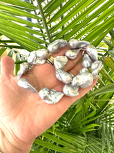 Load image into Gallery viewer, Hand holding a baroque pearl necklace with silver details, showcasing large, iridescent pearls against a green background.