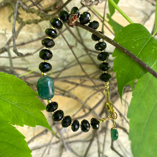 Spinel emerald bracelet featuring black spinel rondelle beads and vibrant green emerald accents among lush leaves.